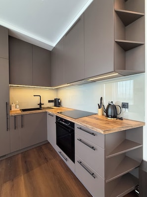 A modern kitchen with grey cabinetry, a wooden countertop, a black dishwasher, and a kettle. - Luxury 2-Bedroom Apartment with Sonos Sound, Wi-Fi, TV, and LED Lighting in Kaunas, Freda (Kaunas)