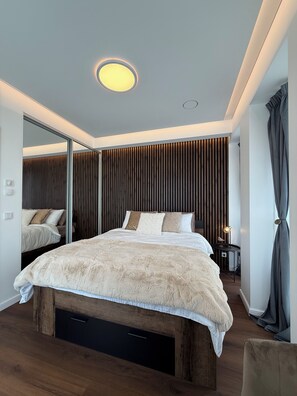 Ein modernes Schlafzimmer mit einem großen Bett, einem Spiegel, einem Nachttisch und einem Beistelltisch.