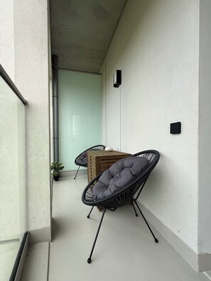A balcony with a wooden table and two chairs, a potted plant, and a wall-mounted light fixture. - Luxury 2-Bedroom Apartment with Sonos Sound, Wi-Fi, TV, and LED Lighting in Kaunas, Freda (Kaunas)