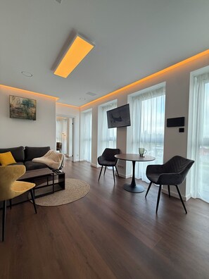 Ein modernes Wohnzimmer mit einer Couch, Sesseln, einem Couchtisch und einem an der Wand befestigten Fernseher.