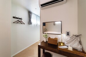 A hotel room with a bed, a bedside table with a lamp, a mirror, a wall-mounted air conditioner, and a window with curtains.