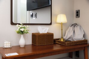 A hotel room's reception area with a mirror, a vase with flowers, a tissue box, a lamp, and a bag.