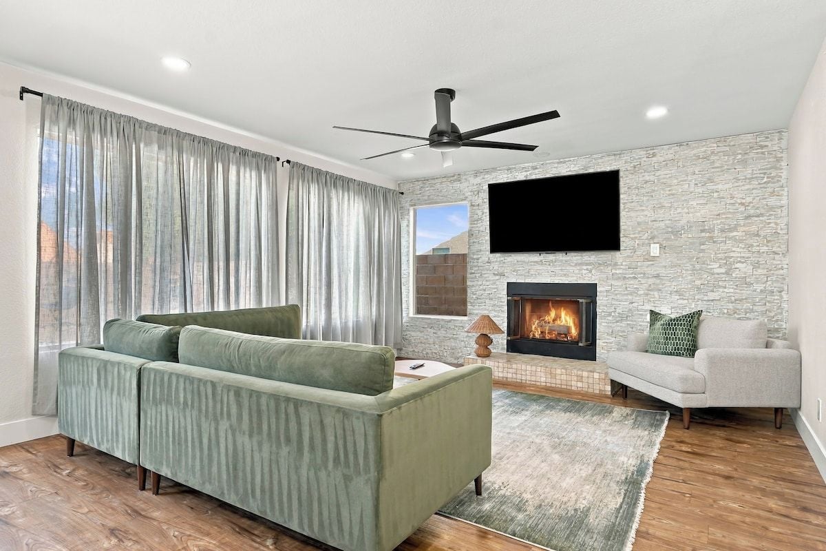 A living room with a green sofa, a fireplace, a flat-screen TV, and a ceiling fan.