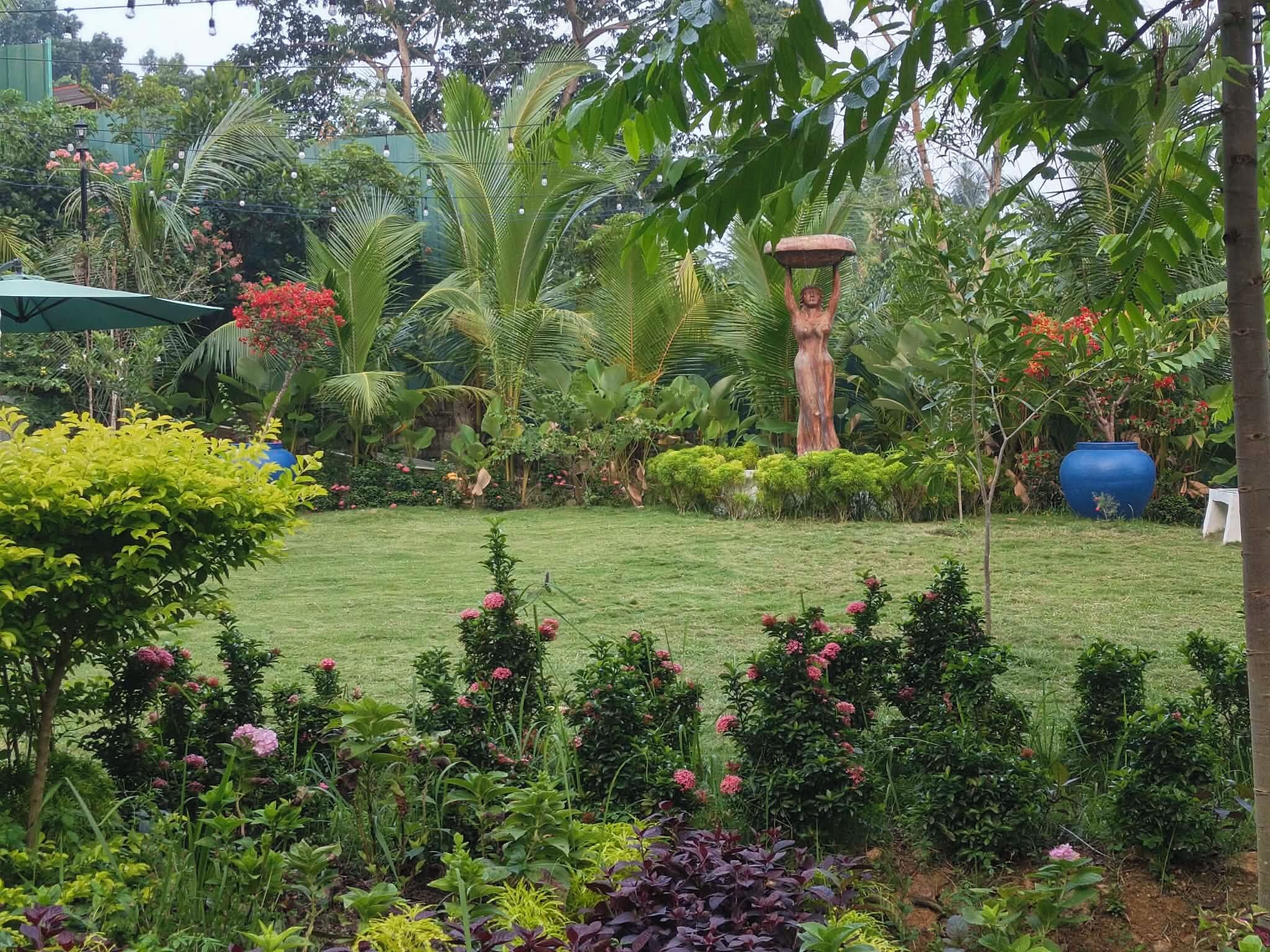 Un jardin luxuriant, avec une grande variété de plantes, une statue centrale et un pot bleu.