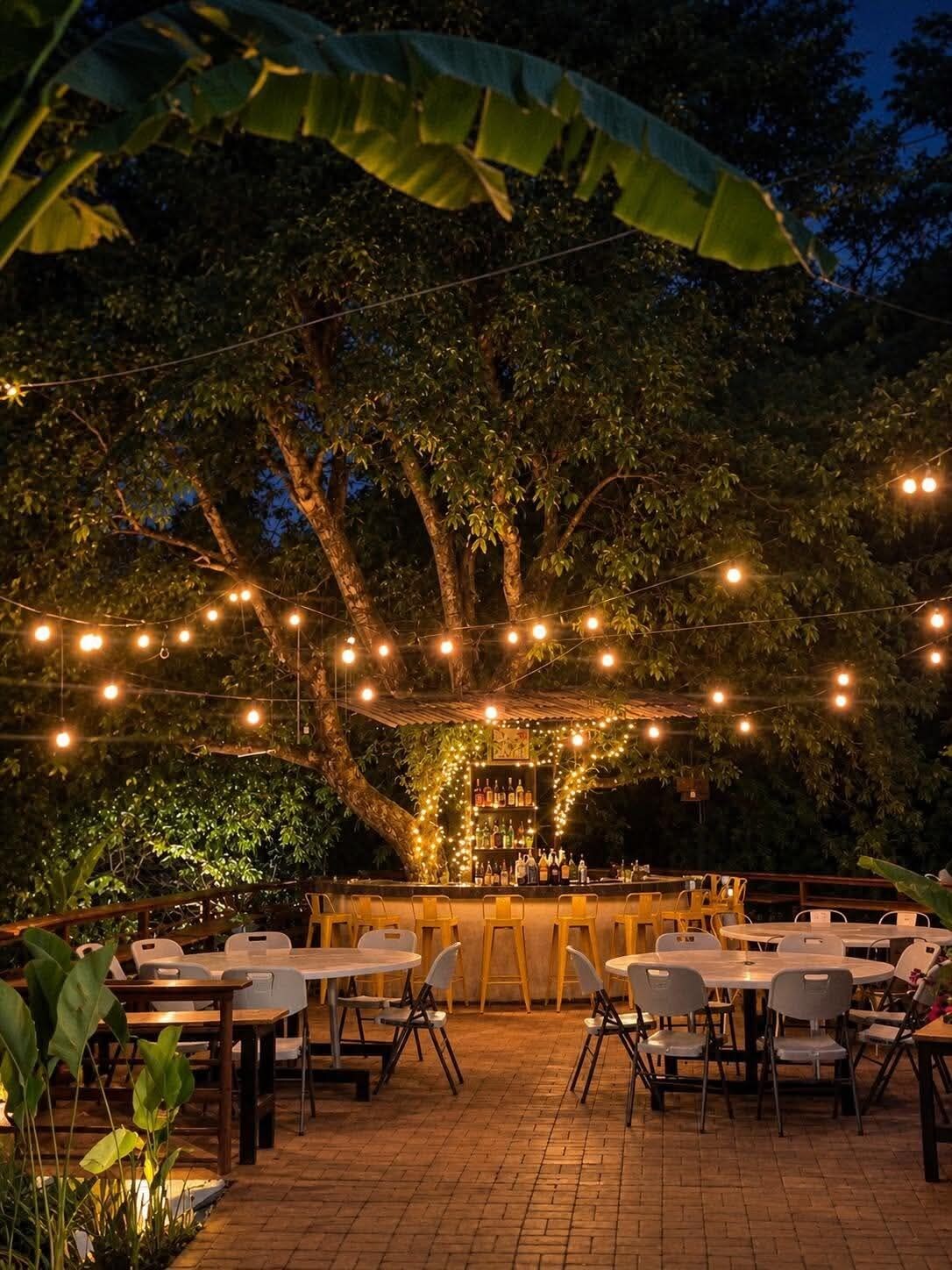 Un espace de restauration en plein air avec des tables et des chaises, des guirlandes lumineuses et un bar où sont exposées des bouteilles.