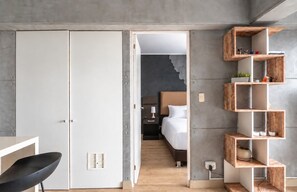 A modern hotel room with a wardrobe, a desk, a chair, a bed, and a built-in wooden shelf unit. - Stylish Ocean View 2BR • King Bed• Pool & Gym (Barranco)