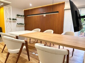 A conference room with a long table, white chairs, a wooden panel wall, and a mounted television. - Stylish Ocean View 2BR • King Bed• Pool & Gym (Barranco)
