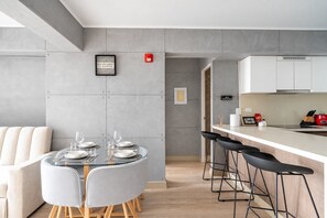 Eine moderne Küche mit Bar, einem Esstisch für vier Personen und einem Sofa im angrenzenden Wohnbereich.