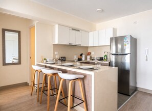 A modern kitchen with a central island, bar stools, stainless steel appliances, and white cabinetry. - Ocean View 2BR Apt • King Bed • Rooftop Pool & Gym (Barranco)