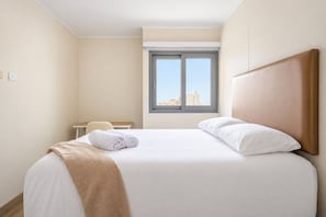 A hotel room with a bed, a desk, and a window with a city view. - Ocean View 2BR Apt • King Bed • Rooftop Pool & Gym (Barranco)
