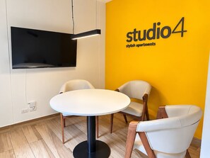 A room with a round table, two chairs, a flat-screen TV mounted on the wall, and a yellow accent wall with the text 'studio4 stylish apartments'. - Ocean View 2BR Apt • King Bed • Rooftop Pool & Gym (Barranco)