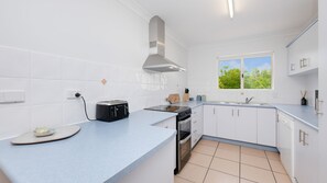 A modern kitchen with white cabinets, a built-in oven, a gas stove, and a window with a view of trees.