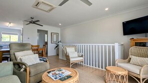 A spacious living area with wicker furniture, a television, and a balcony with a white railing. - Beautifully renovated pet friendly home in tropical gardens with stunning beachfront views (Horseshoe Bay)