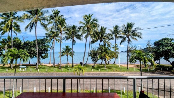 A view from a balcony with a railing, overlooking a beach with palm trees and the ocean.