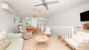 A spacious living area with a ceiling fan, a dining table with chairs, and a television mounted on the wall.