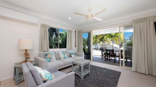 A modern living room with a grey sofa, a small table, and a ceiling fan.