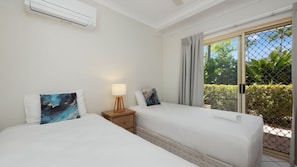 A hotel room with two beds, a nightstand with a lamp, and a sliding glass door to a balcony.