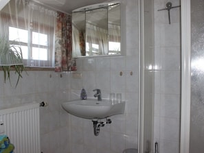 A bathroom with a white sink, a mirror, a shower, and a radiator. - Holiday Apartment With 2 Bedrooms (Rosshaupten)
