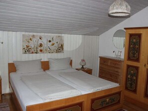 A bedroom with a double bed, a wooden dresser, a mirror, and a floral artwork on the wall. - Holiday Apartment With 2 Bedrooms (Rosshaupten)