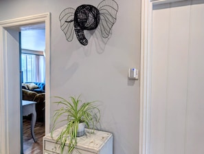 Un pasillo con un cuadro decorativo de un elefante, una planta en maceta y una puerta que da a una habitación con un sofá azul.