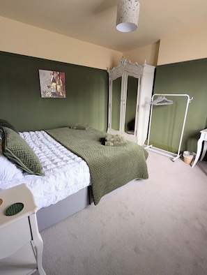 Un dormitorio con cama, armario, espejo, perchero y un cuadro en la pared.