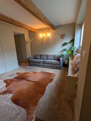 Una habitación con suelo de piedra, un sofá estampado, un tapete de cuero de vaca, una decoración de cabeza de ciervo montada en la pared y una planta en maceta.
