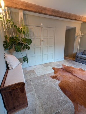 A room with a stone floor, a wooden bench, a cowhide rug, a door, and hanging plants.