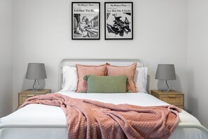 Une chambre à coucher comprenant un lit, deux tables de chevet, deux lampes fixées au mur et deux tableaux encadrés accrochés au mur.