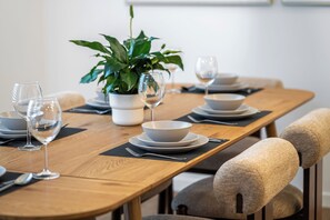 Una mesa de comedor dispuesta con platos, tazones y copas de vino, junto con una planta en maceta.