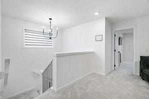 Ein helles, weißes Interieur mit einer Treppe, einem Chandelier und einer gerahmten architektonischen Zeichnung an der Wand.
