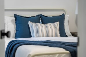 Una cama con ropa de cama blanca y azul, una almohada a rayas y una manta azul.
