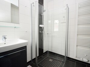 Ein modernes Badezimmer mit einer gläsernen Duschkabine, einem weißen Waschbecken und einem Handtuchhalter.