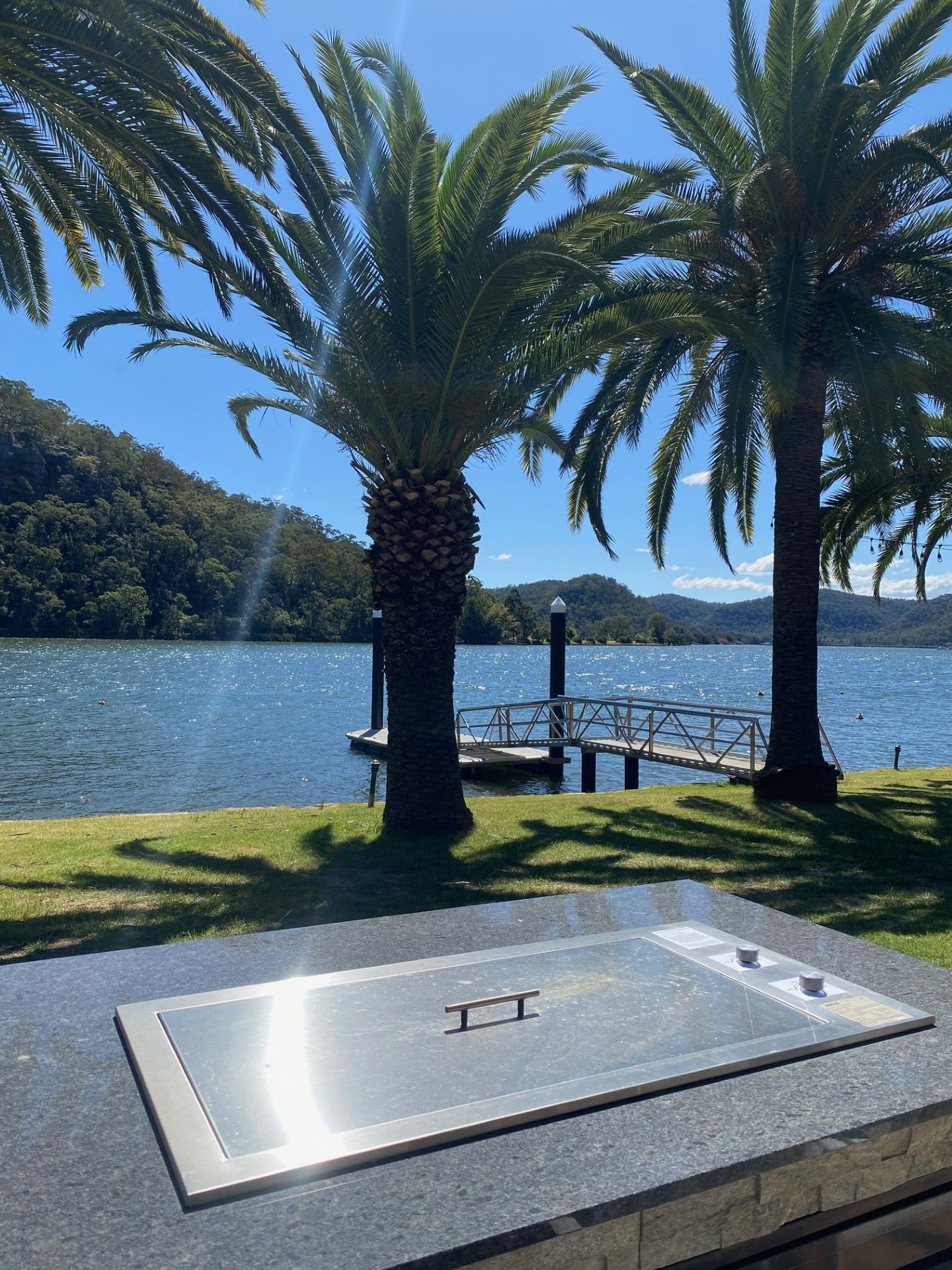 Une vue sur le lac, avec des palmiers, un quai et un banc en pierre.
