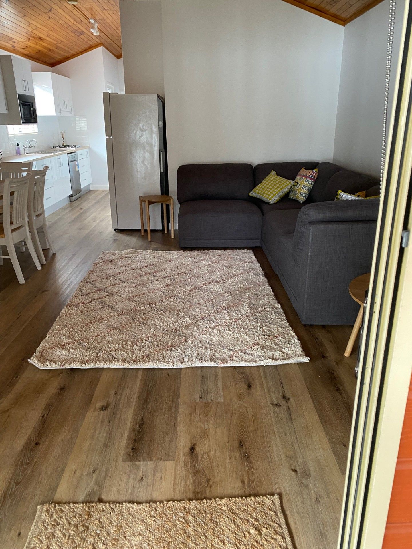 A living room with a sofa, a rug, and a kitchen in the background.