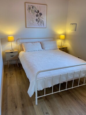 A bedroom with a metal bed frame, white bedding, two bedside tables with lamps, and a wall-mounted light switch. - Cabin in Tasman Holiday Park Wisemans Ferry  Sleeps 8 (Wisemans Ferry)