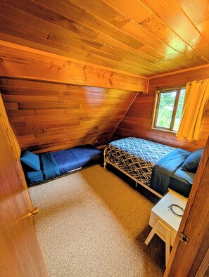 A room with a sloped ceiling, a bed with a patterned bedspread, a small white table, and a window with curtains. - Cozy Chalet in the Heart of Girdwood (Anchorage)