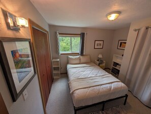 Une chambre à coucher avec un lit, une table de chevet, une lampe et une fenêtre avec des rideaux.