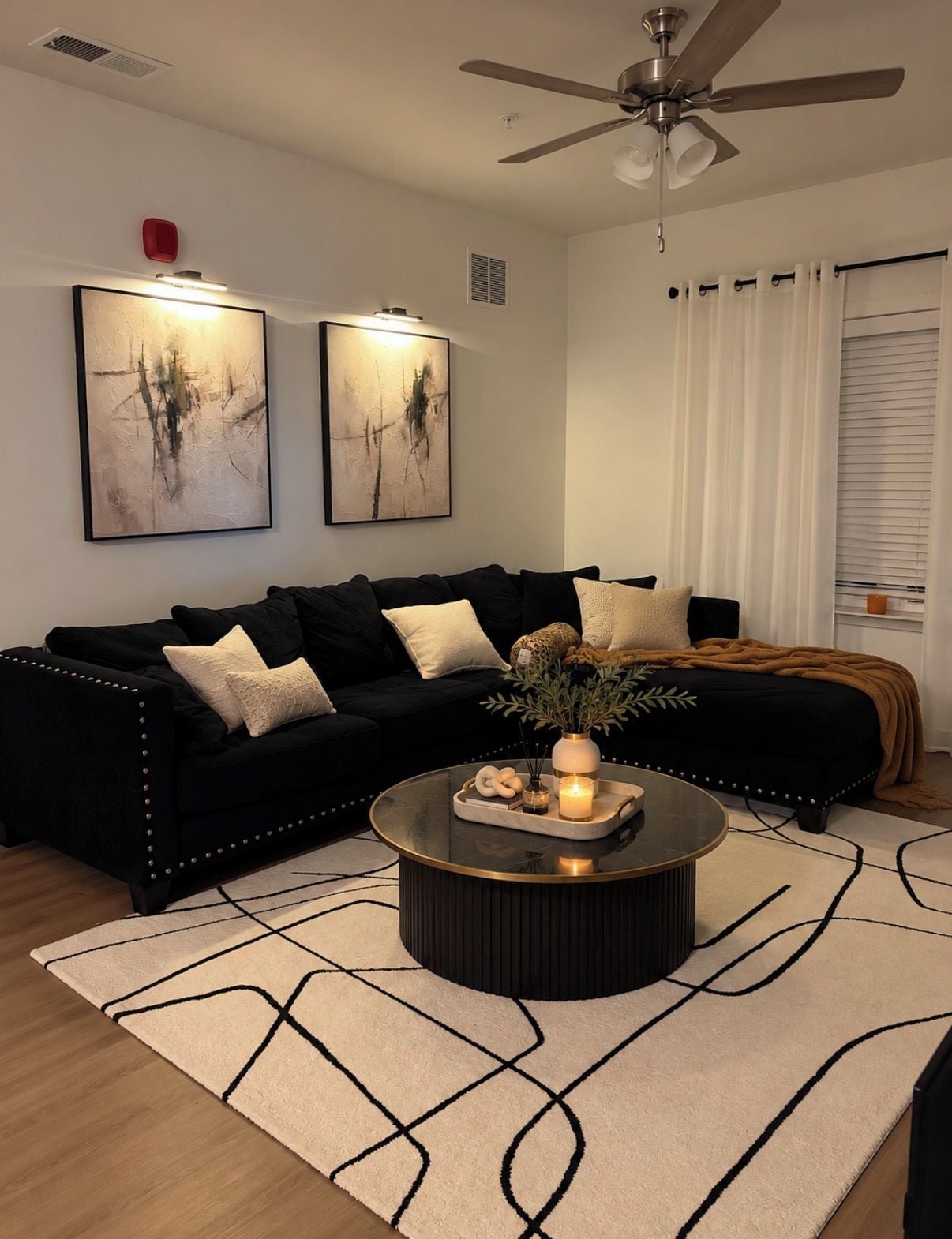 A modern living room with a black sofa, a round coffee table, and two abstract paintings on the wall.