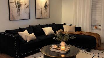 A modern living room with a black sofa, a round coffee table, and two abstract paintings on the wall.