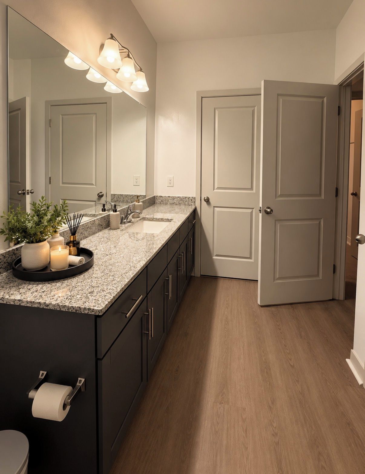 A modern bathroom with a granite countertop, a large mirror, a vanity with a sink, and a toilet.