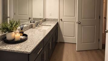A modern bathroom with a granite countertop, a large mirror, a vanity with a sink, and a toilet.