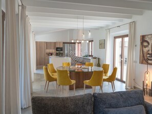 Un saló modern amb una taula rodona de vidre i cadires grogues, un sofà gris i una cuina al fons.