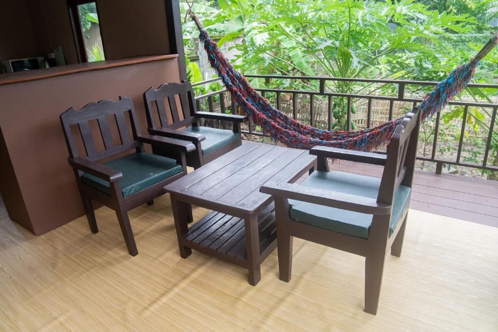 A wooden deck with a table and two chairs, a hammock, and a view of greenery.