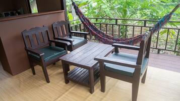 A wooden deck with a table and two chairs, a hammock, and a view of greenery.