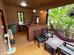 Una habitación con una mesa y sillas de madera, una kitchenette pequeña y vistas a un verdor exuberante a través de un ventanal amplio.