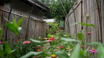 Een smal tuinpad, begrensd door bamboomschermen, dat naar een huis met een schuin dak leidt.