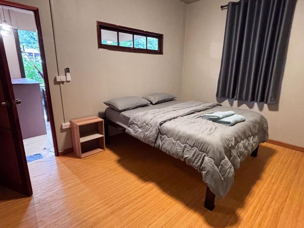 A bedroom with a bed, a small bedside table, a window with a view, and a door leading to another room.