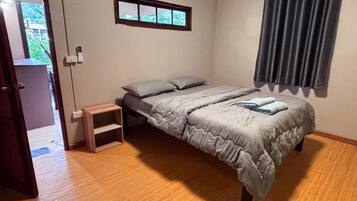 A bedroom with a bed, a small bedside table, a window with a view, and a door leading to another room.