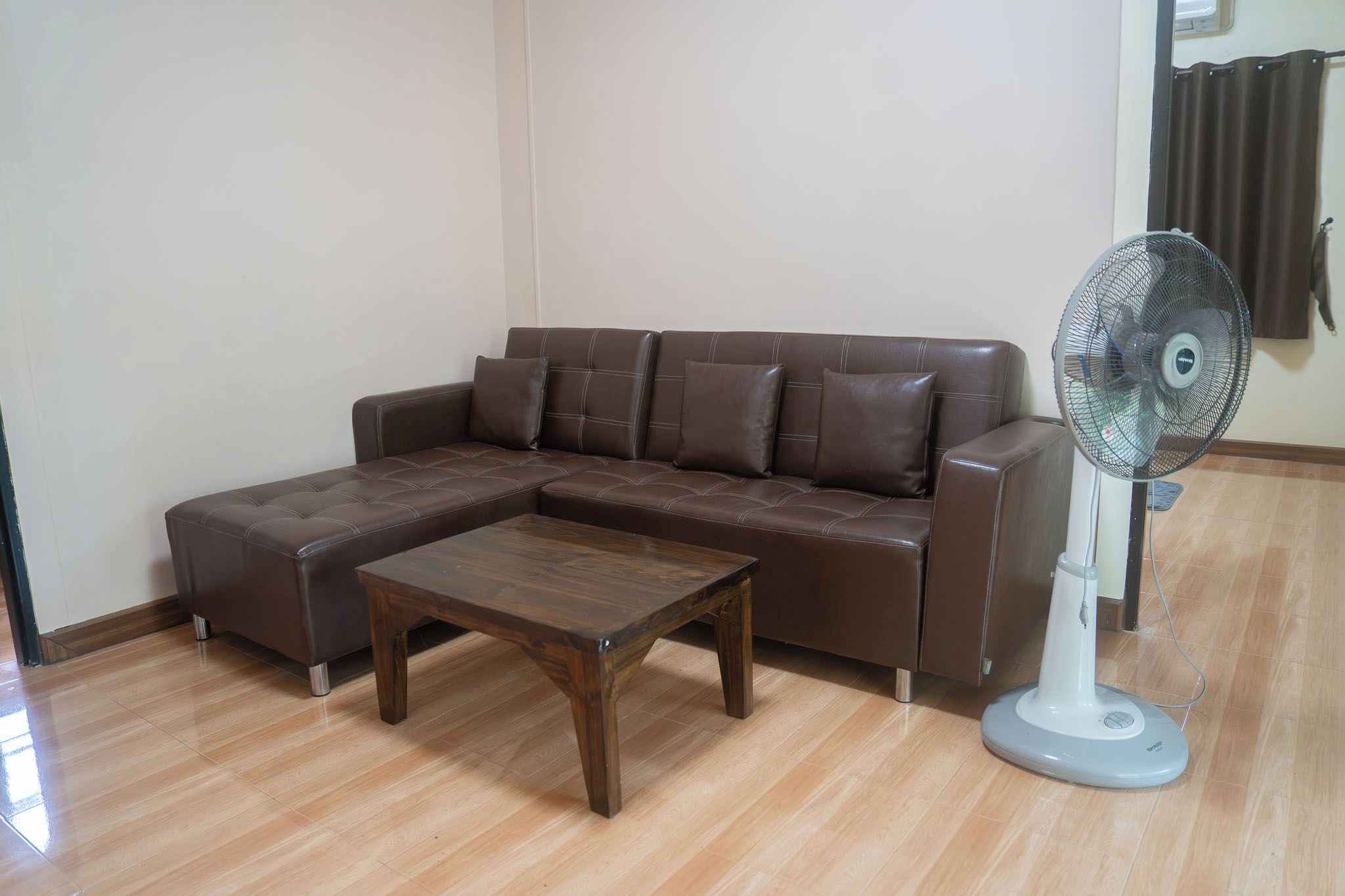 A living room with a brown leather sofa, a wooden coffee table, and a standing fan.
