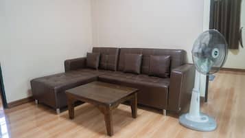 A living room with a brown leather sofa, a wooden coffee table, and a standing fan.